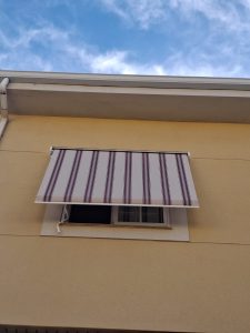 Detalle de un toldo manual con lona acrílica de rayas y brazos de punto recto.